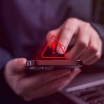 10DLC Regulations - Red triangle exclamation point alert over someone typing on their phone